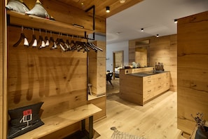 A wooden interior with a clothing rack, a bench, a mirror, and a kitchen area. - 8020 Alpine Residence 20 (Schröcken)