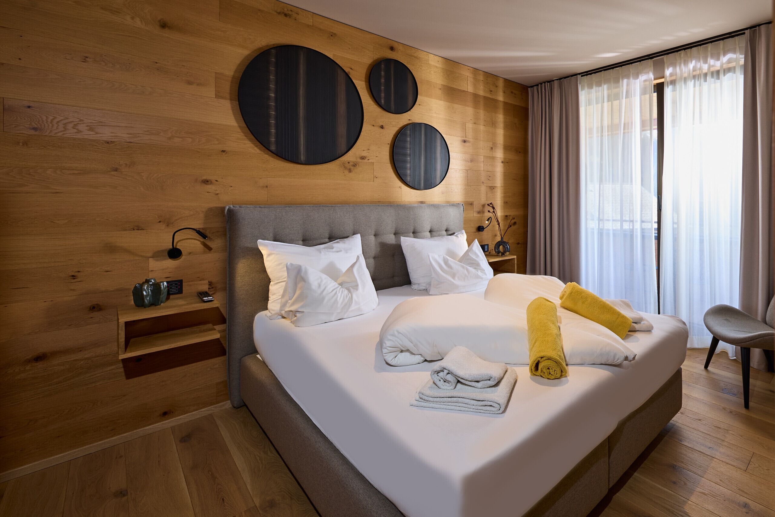 Ein Hotelzimmer mit einem großen Bett, einem Holzkopfende und Blick ins Freie durch ein Fenster.