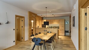 A modern kitchen with wooden cabinets and a central island, a dining area with a wooden table and chairs, and a hallway with wooden flooring. - 8020 Alpine Residence 20 (Schröcken)