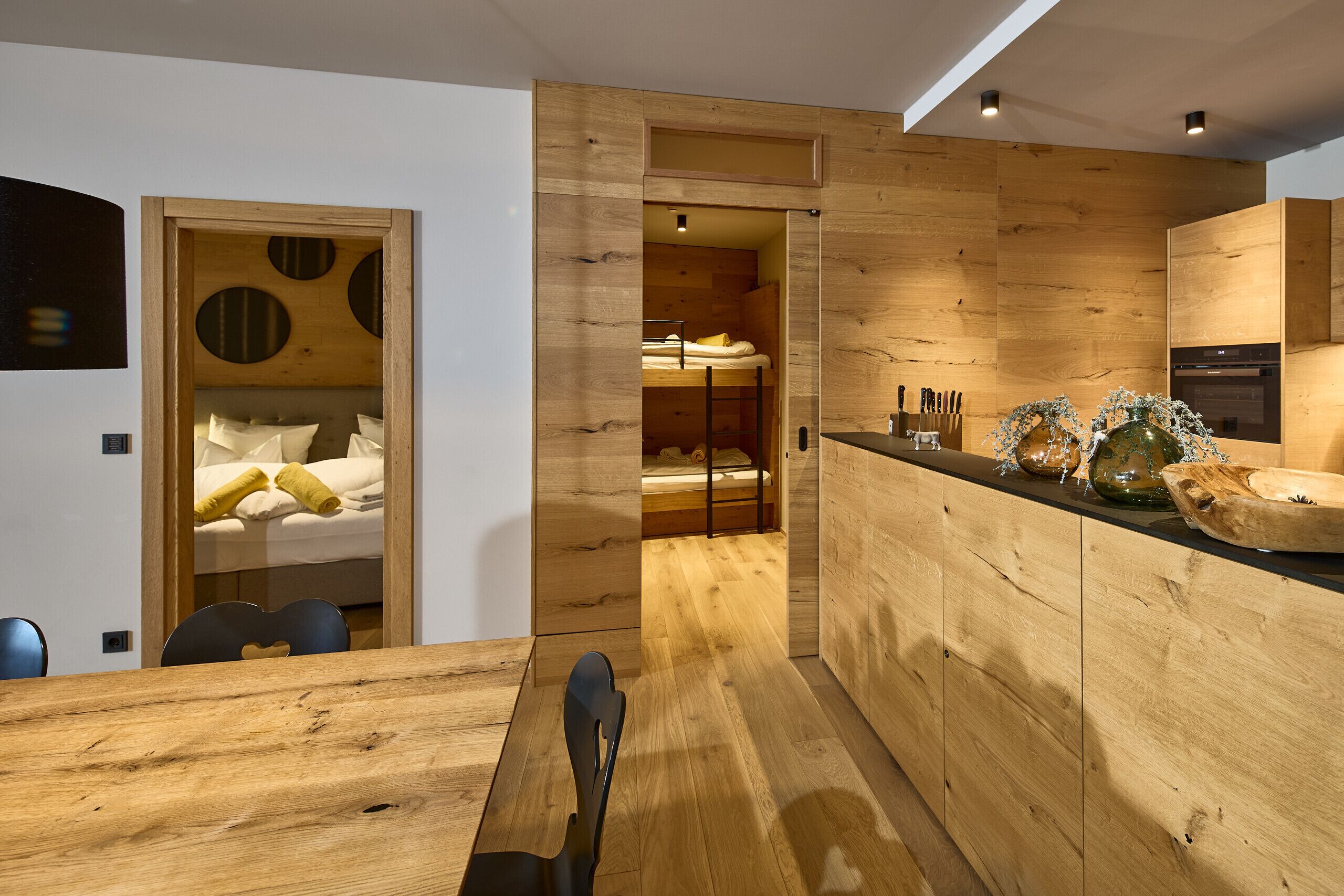 Una cocina moderna con armarios de madera, un comedor con mesa de madera y una zona de descanso separada con literas.