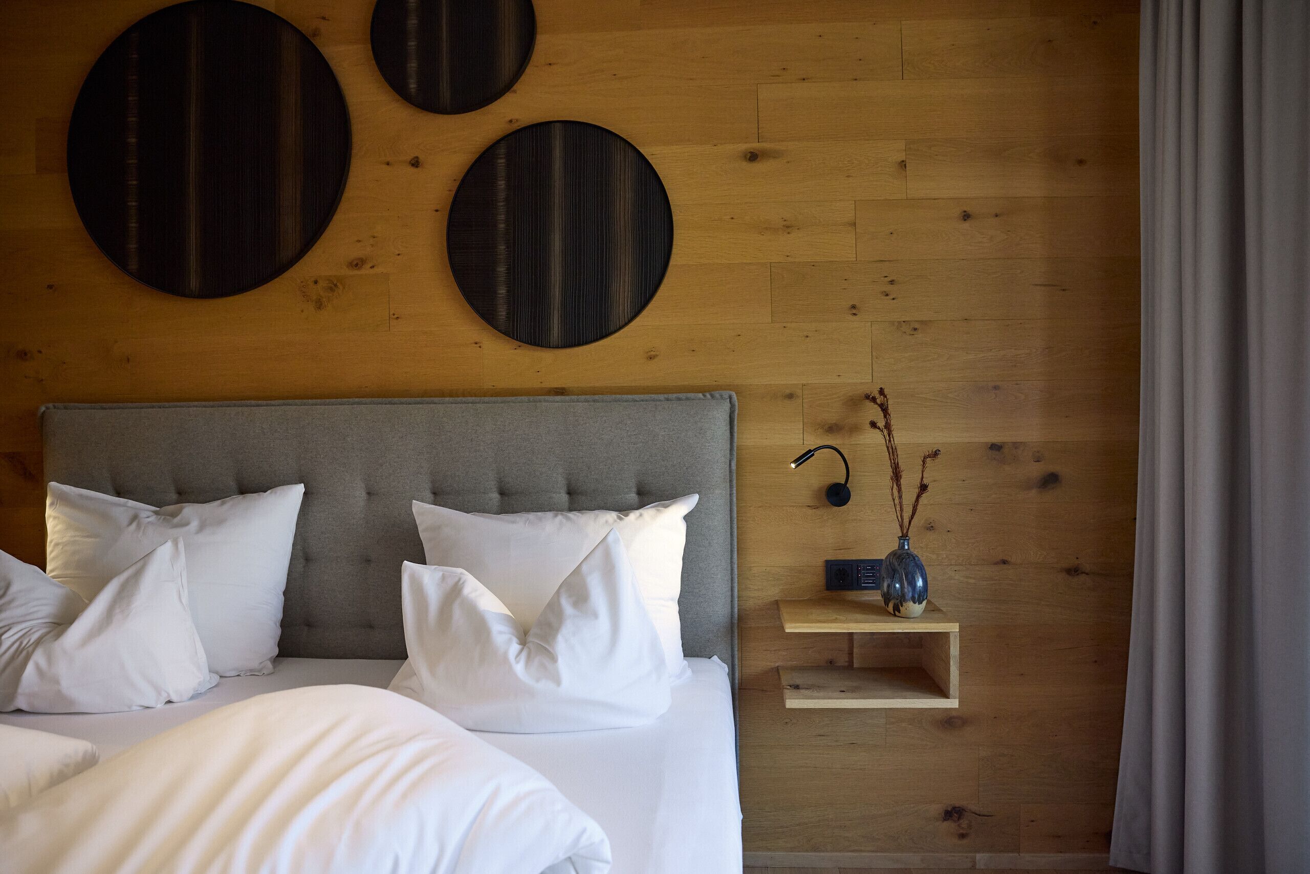 A bedroom with a bed, pillows, a bedside table with a lamp, and wall decorations.