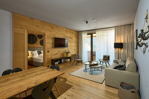 Ein modernes Wohnzimmer mit Holzboden, einer Couch, einem Esstisch und einem an der Wand befestigten Fernseher.