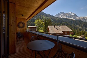 A wooden balcony with a table and chairs, overlooking a mountainous landscape with a clear sky. - 8020 Alpine Residence 20 (Schröcken)