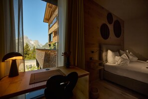 Ein Schlafzimmer mit einem Bett, einem Schreibtisch mit Lampe und Blick auf Berge durch ein Fenster.