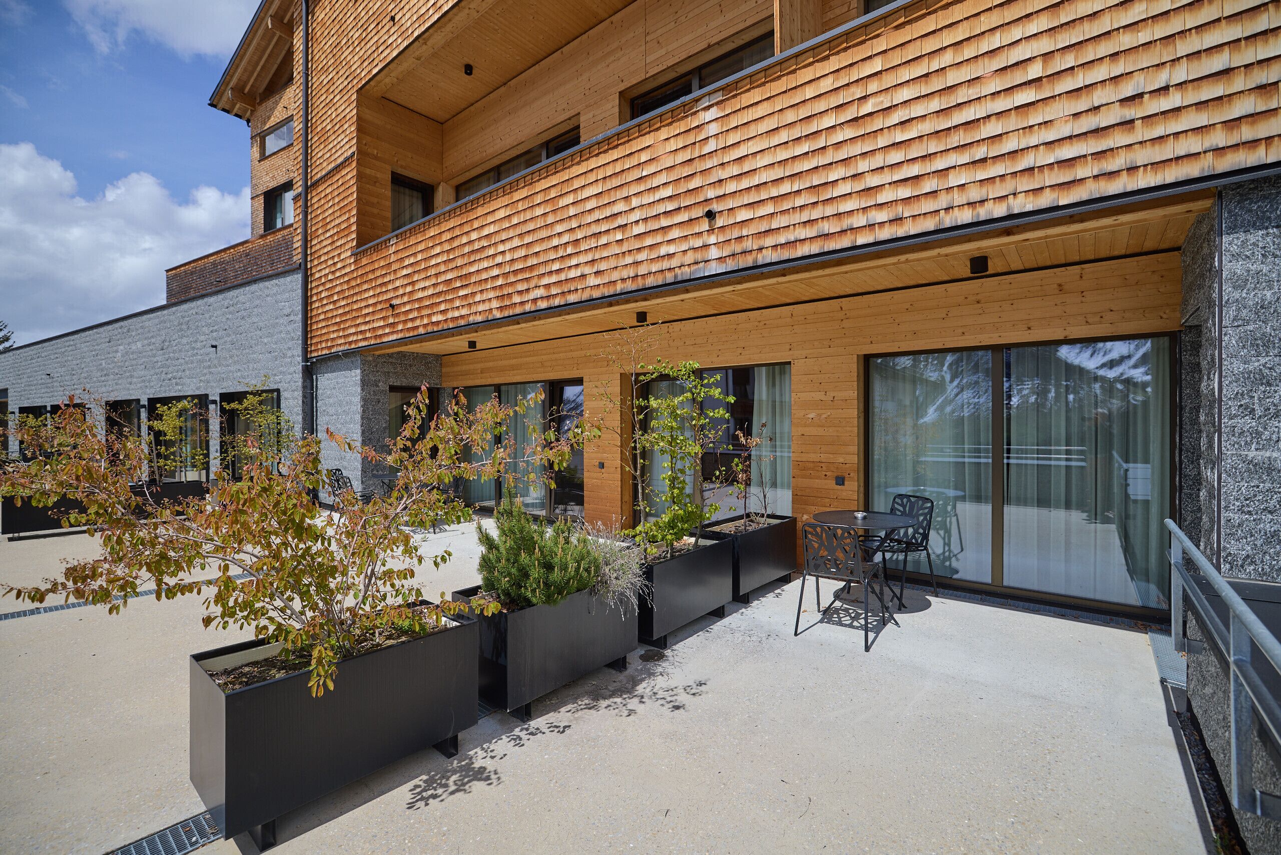 Ein modernes Gebäude mit Holzfassade, einer Sitzgelegenheit im Freien und großen Fenstern.