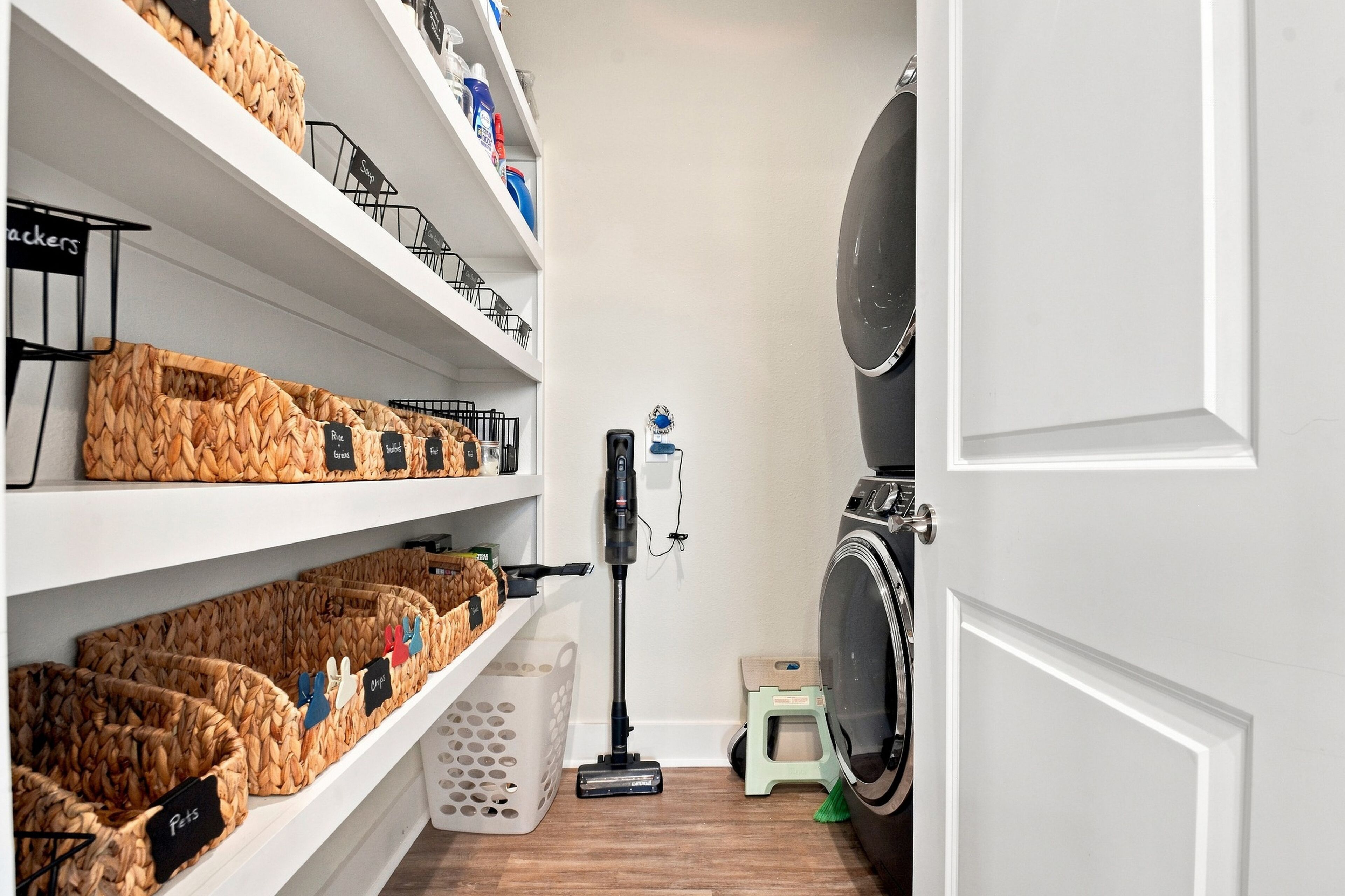 A laundry area with shelves labeled for different items, a vacuum cleaner, and a washing machine.