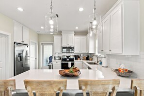 A modern kitchen with white cabinets, stainless steel appliances, and a large island with chairs. - Sausalito Beach Retreat | Pool | Beach | Relax (Galveston)
