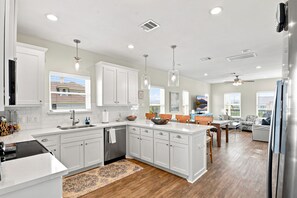 A modern kitchen with white cabinetry, a central island, and a dining area with a view. - Sausalito Beach Retreat | Pool | Beach | Relax (Galveston)