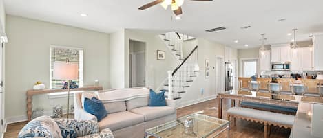 A spacious living room with a modern ceiling fan, a staircase, and a kitchen area.