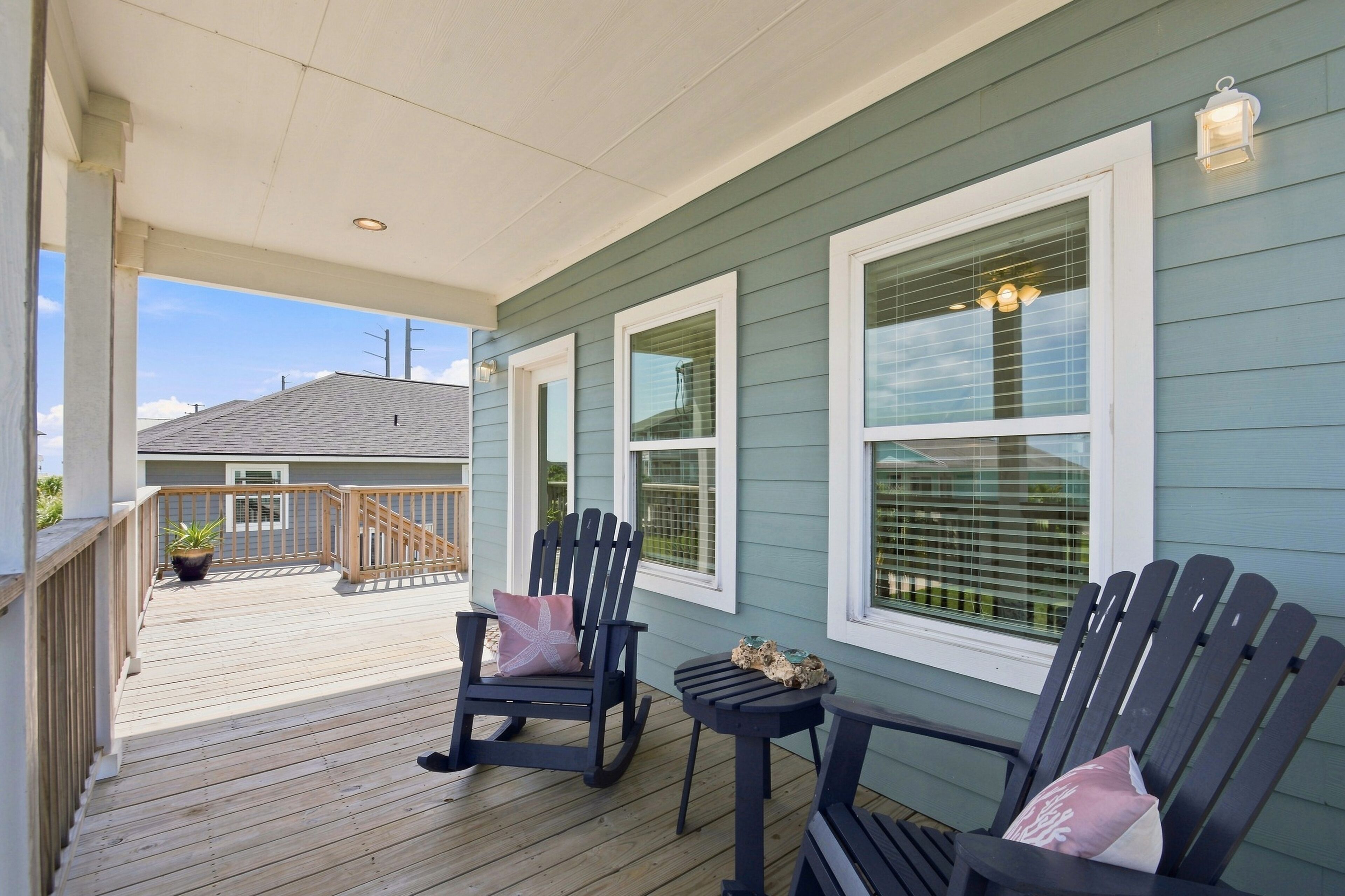 A covered porch with two Adirondack chairs, a small table, and a potted plant.