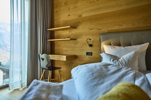 Ein Schlafzimmer mit einem Bett, einem Schreibtisch und einem Stuhl. Ein Fenster mit Vorhängen bietet Blick ins Freie.