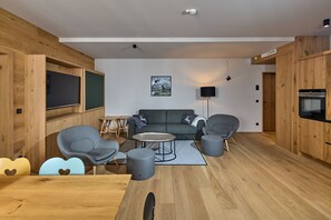 Una sala de estar moderna con piso de madera, un sofá gris, dos sillones grises, una mesa de centro redonda y un televisor de pantalla plana montado en un mueble de madera.