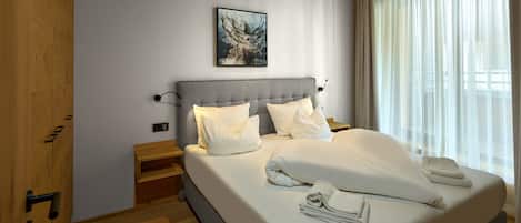 A modern bedroom with a large bed, a headboard, a bedside table, a nightstand, a painting on the wall, and a window with curtains.