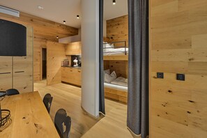 A modern, compact room with a bunk bed, a dining area with a wooden table and chairs, and a kitchenette with a toaster and kettle. - 8023 Alpin Retreat Grand 23 (Schröcken)