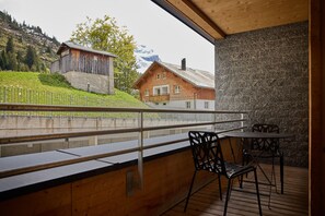 A balcony with a view of a mountain, a wooden building, and a stone wall. - 8023 Alpin Retreat Grand 23 (Schröcken)