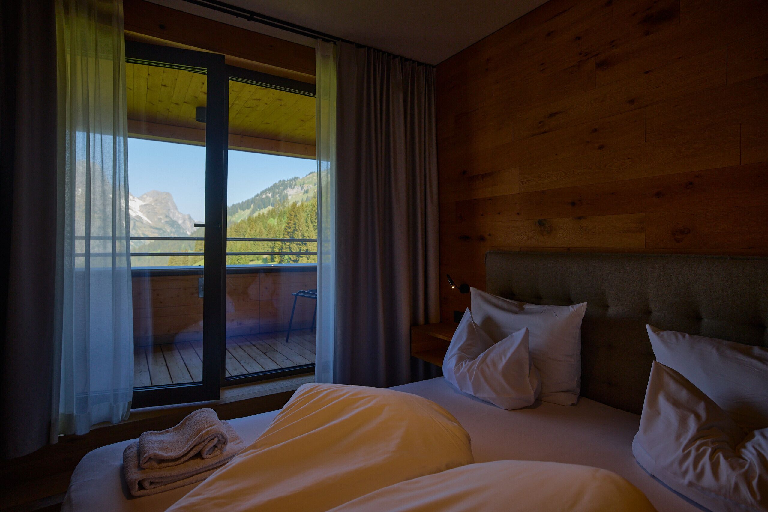 Habitació d'hotel amb un llit, almoines, una finestra amb cortines i vista a les muntanyes.