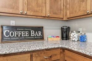A kitchen with wooden cabinets, a coffee maker, and a sign indicating a coffee bar offering coffee, espresso, latte, cappuccino, and macchiato. - The Gathering House On May (Fort Smith)