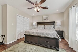 Une chambre à coucher comprenant un lit, des tables de chevet, un ventilateur de plafond, un grand placard et un tableau encadré accroché au mur.