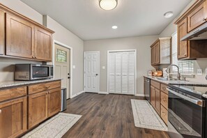 A kitchen with wooden cabinets, a microwave, a dishwasher, and a sink. - The Gathering House On May (Fort Smith)