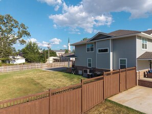 A residential area with a two-story house, a fenced yard, and a church in the background. - The Gathering House On May (Fort Smith)