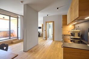 Una cocina moderna con cafetera espresso integrada, piso de madera y puerta corrediza de vidrio que da a un espacio exterior.