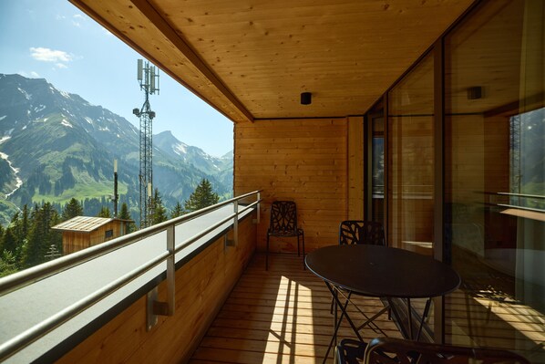 A wooden balcony with a table and chairs, overlooking a mountainous landscape. - 8027 Summit Residence 27 (Schröcken)