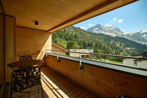 A wooden balcony with a table and chairs, overlooking a mountainous landscape. - 8027 Summit Residence 27 (Schröcken)