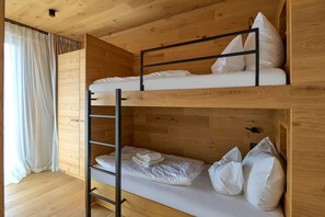 Una cama individual superpuesta con escalera, ropa de cama blanca y cabecera de madera.