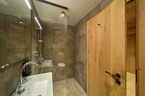 A modern bathroom with a glass shower enclosure, a white sink, and a wooden door. - 8027 Summit Residence 27 (Schröcken)