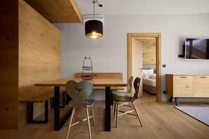 A modern interior with a wooden dining table, two chairs, a hanging light fixture, a television on the wall, and a wooden cabinet. - 8029 Alpine Residence 29 (Schröcken)
