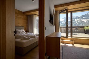Ein Schlafzimmer mit Bett, Schreibtisch und Blick auf Berge durch große Fenster.