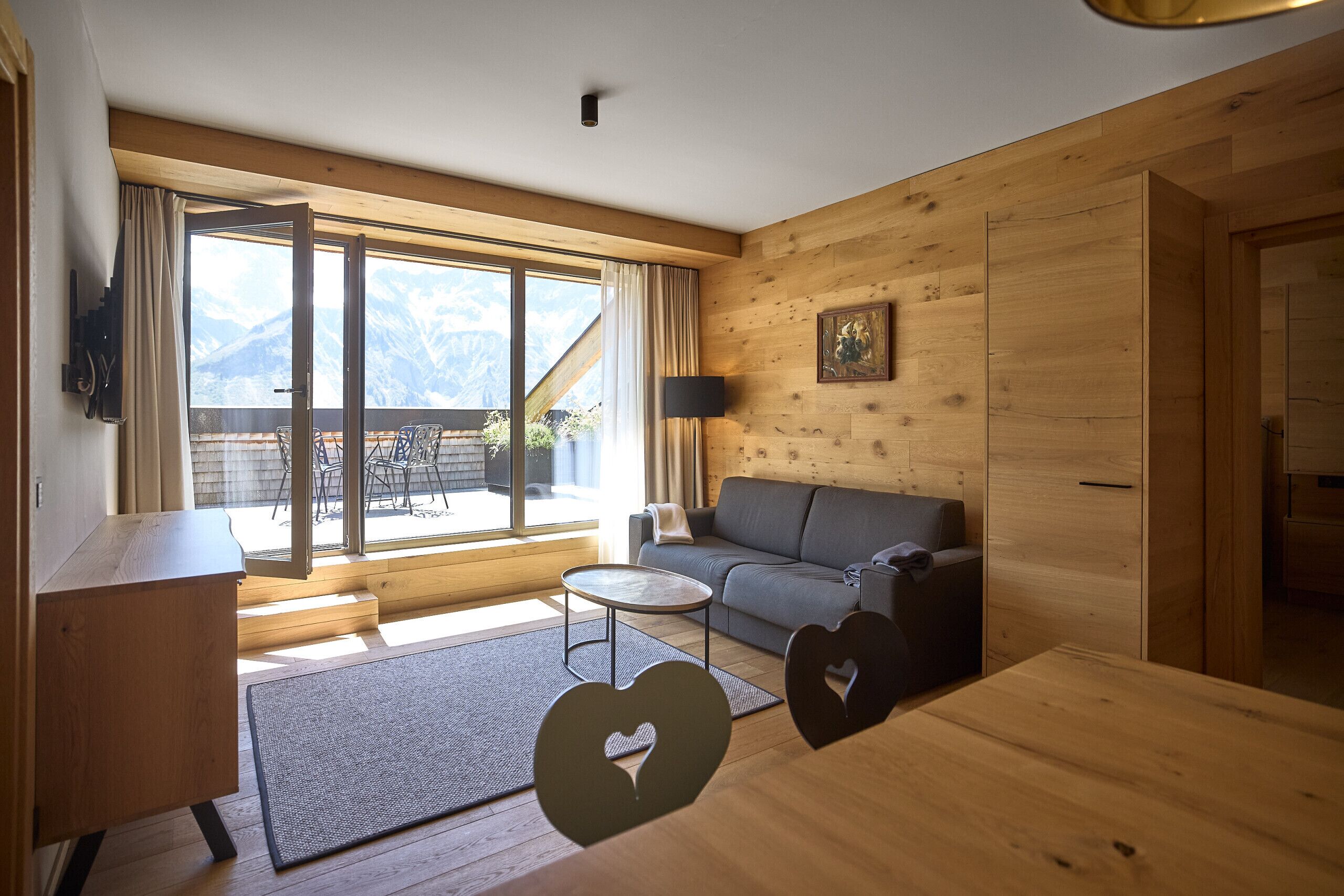Una sala de estar moderna con un sofá, una mesa de centro y vistas a montañas a través de amplios ventanales.