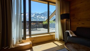 Ein Zimmer mit großem Fenster, Holzboden, einer Couch, einer Lampe und Bergblick.