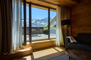 Ein Zimmer mit großem Fenster, Holzboden, einer Couch, einer Lampe und Bergblick.