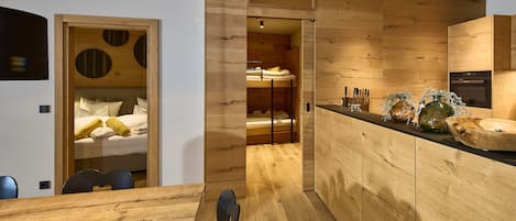 Eine moderne Küche mit Holzschränken, ein Essbereich mit Holztisch und ein separater Schlafbereich mit Etagenbett.