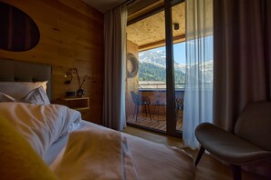 Ein Hotelzimmer mit Bett, Sessel, Tisch und Bergblick durch ein großes Fenster.