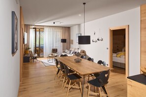 Ein stilvoller Wohnraum mit Esstisch aus Holz, schwarzen Stühlen, einer Couch und einem an der Wand befestigten Fernseher.