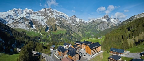 A mountain resort with chalet-style buildings, a ski lift, and snow-capped peaks in the background.