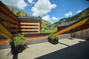 Ein modernes Gebäude mit einem geneigten Dach, Holzbalkonen und Blick auf eine gebirgige Landschaft.