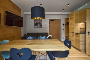 Ein moderner Essbereich mit einem Holztisch, herzförmigen Stühlen, einem an der Wand befestigten Fernseher und einer Pendelleuchte.