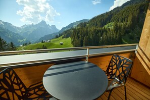 Ein Balkon mit Tisch und Stühlen, der auf eine gebirgige Landschaft mit einer Straße und Gebäuden blickt.