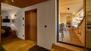 A wooden interior with a staircase leading to an upper level, a seating area with a table and chairs, and a door with a handle. - 8036 Alpine Residence 36 (Schröcken)