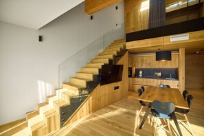 A modern interior with a wooden staircase, a dining area with a wooden table and chairs, and a kitchen with wooden cabinets and a black countertop. - 8038 Alpin Retreat Grand Maisonette 38 (Schröcken)
