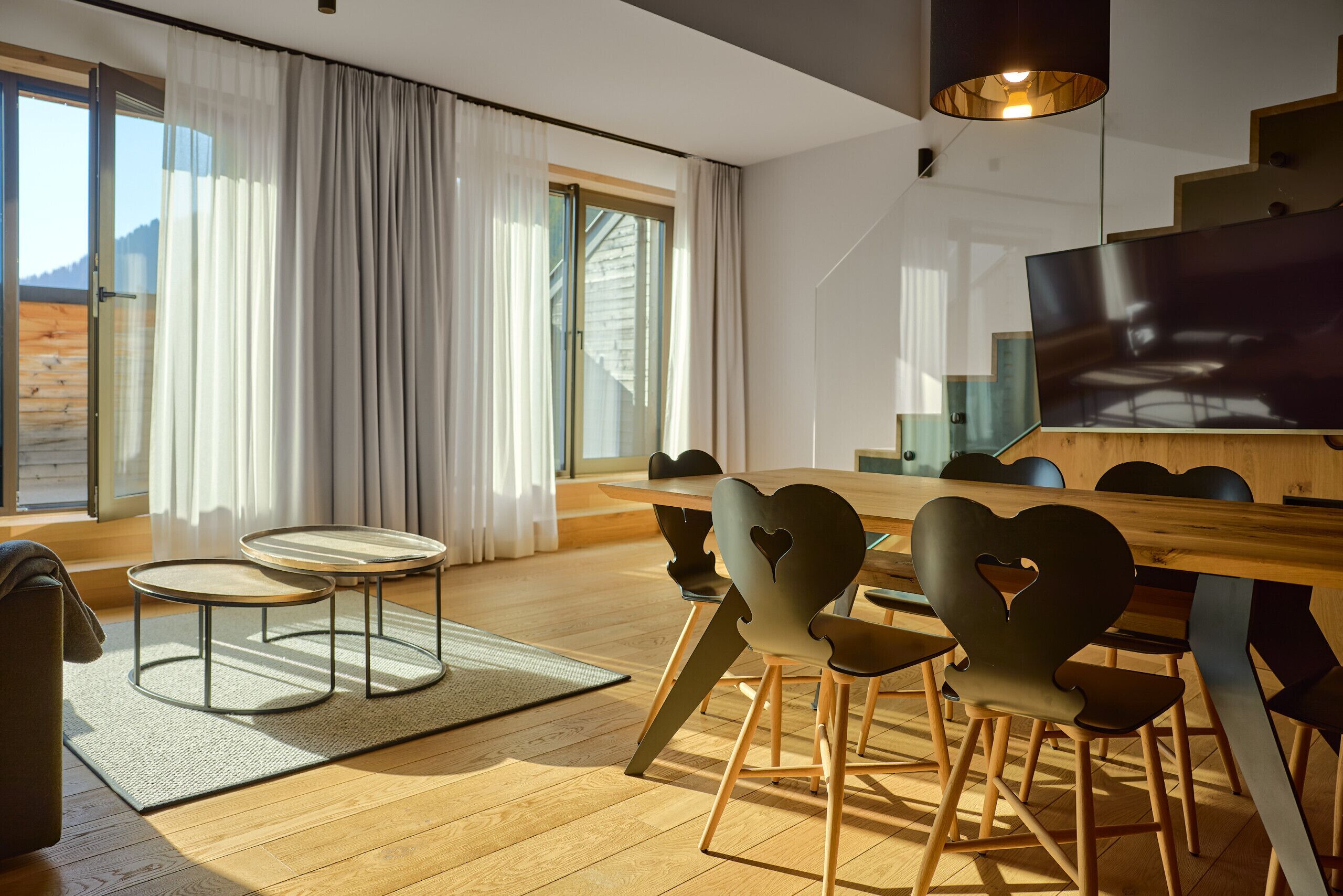 A modern living room with a wooden floor, a round coffee table, a sofa, and a dining area with a wooden table and heart-shaped chairs.