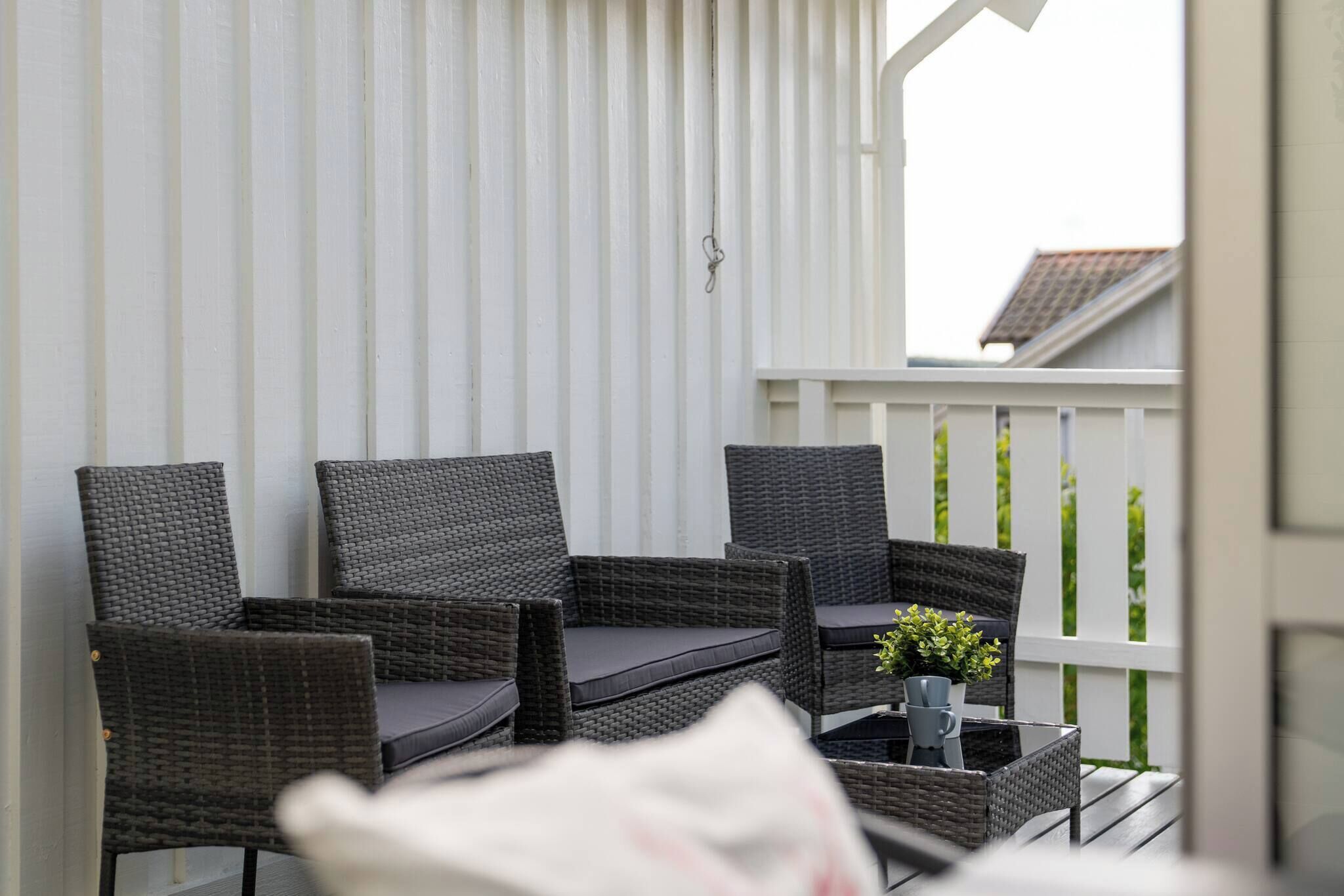 A balcony with wicker furniture, a small table with a plant, and a white railing.
