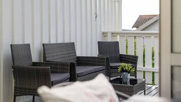 A balcony with wicker furniture, a small table with a plant, and a white railing.