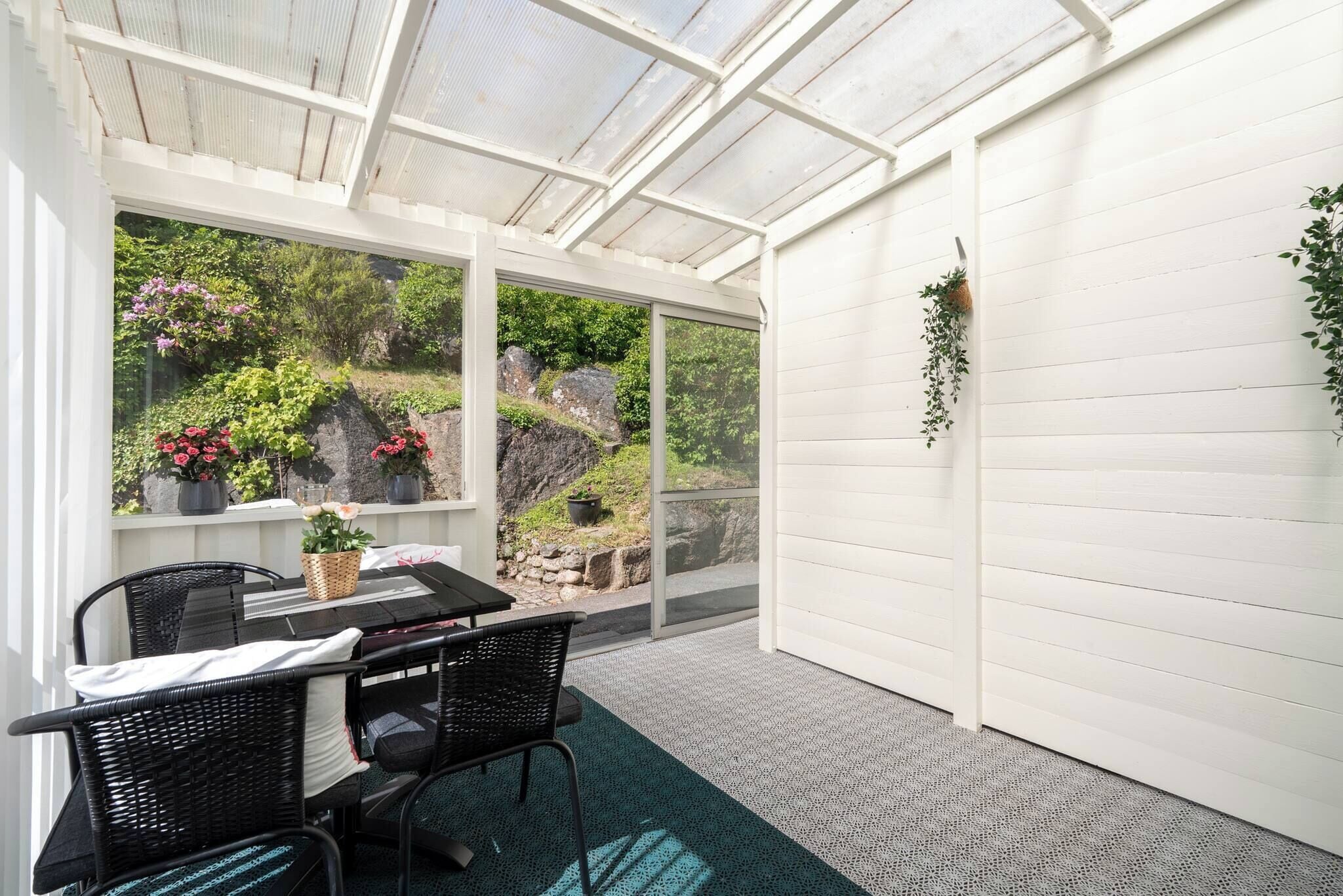 A covered patio with a table and chairs, large windows, and potted plants.