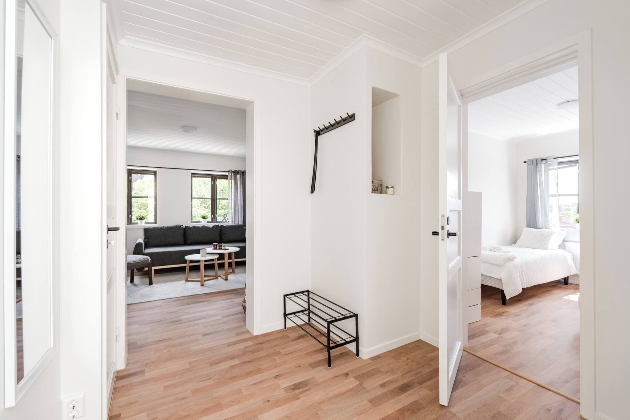A spacious room with a wooden floor, a black metal rack, a grey sofa, and a white bed.
