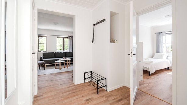 A spacious room with a wooden floor, a black metal rack, a grey sofa, and a white bed. - Linneby , fri Parkering (Uddevalla)