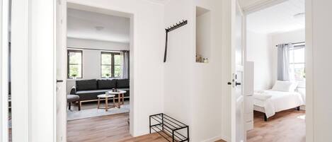 A spacious room with a wooden floor, a black metal rack, a grey sofa, and a white bed.